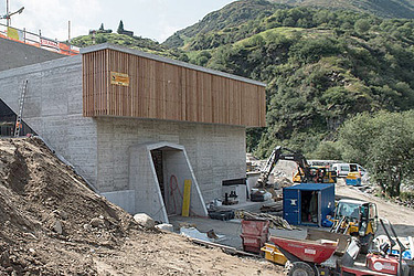 STRABAG - Baustelle im Kraftwerksbau mit Betonbauwerk am Hang, umgeben von Baumaschinen und Materiallien.
