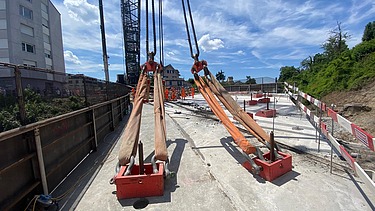 Zwei grosse Ankerschuhe sind mit Schlaufenseilen am Fangkran befestigt und liegen bereit auf der Baustelle für den Brückenaushub.
