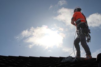 Mann steht auch dem Dach in Sicherheitskleidung bei Sonnenschein mit leichtere Bewölkung