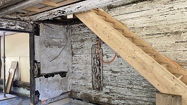 Ein Treppe aus hellem neuen Holz im Adlisberghof mit alten, abblätternden Wänden und Holzbalken.