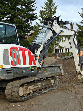 Weisser Bagger von STRABAG beim Abtragen eines Erd- oder Aushubhügels auf einer Baustelle.