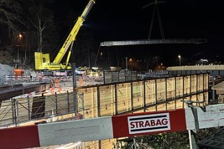 Im Vordergrund STRABAG Absperr-Latten im Hintergrund ein Kran der ein  24 Tonnen Stahlträger hebt