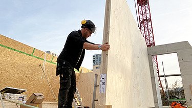 Einsetzen eines Holzelements durch einen Kran und einem STRABAG Mitarbeiter