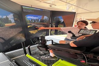 Eine Lernende in STRABAG T-Shirt zeigt Besucher wie man den Bagger-Simulator steuert.