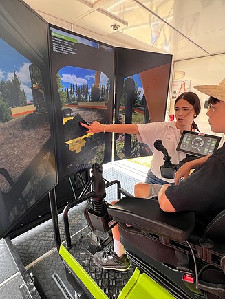 Eine Lernende in STRABAG T-Shirt zeigt Besucher wie man den Bagger-Simulator steuert.