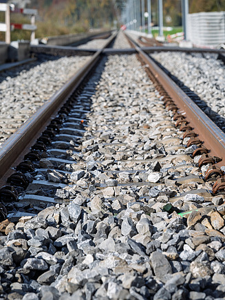 Nahaufnahme eines Bahngleises im Hintergrund sind Bauarbeiten und Geräte entlang der Strecke zu erkennen.