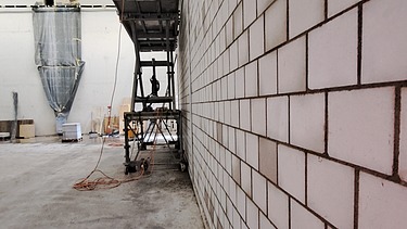 Innenansicht einer Baustelle mit einer grossen Kalksandsteinwand und einer Scherenbühne in einer Logistik Halle.