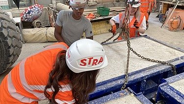 Drei Lernende befestigen dicke Ketten an einem Betonelement