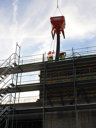 Baustelle mit Arbeiter, der Beton aus einem Kübel aufs Gerüst spritzt.
