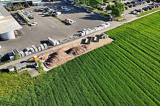 Drohnenaufnahme vom Installationsplatz neben Landi-Parkplatz und einem grünen Feld mit Baumaterial.