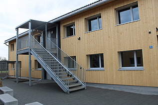 Asylunterkunft aus Holz, zweistöckig mit Metalltreppe und Geländer. 