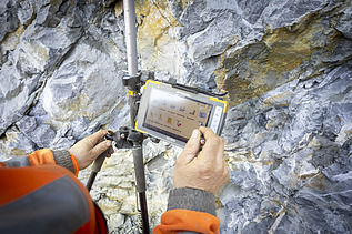 Ein STRABAG-Mitarbeiter hält ein digitales Vermessungsgerät an einer Felswand und misst präzise die Struktur des Gesteins.