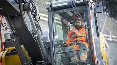 Nahaufnahme eines Baggerfahrers in der Kabine eines Baggers, der in der Baugrube an der Axenstrasse arbeitet.