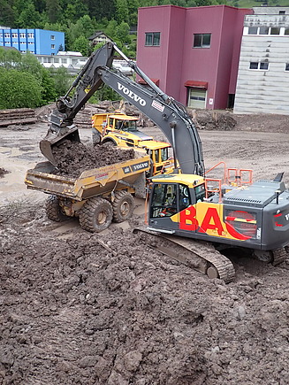 STRABAG-Bagger belädt Lastwagen mit Schlammmassen 