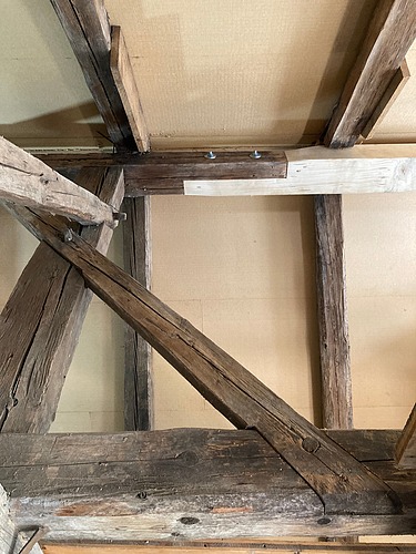 Blick in einen Dachstuhl mit Holzbalken und Verkleidung, links ist ein Gerüst zu sehen. Eine Kombination aus altem vorhandenem Holz mit neuem Holzelementen. 