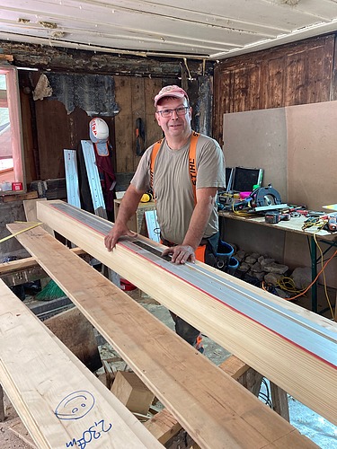 Der Polier arbeitet an einem Holzbalken und blickt lächelnd in die Kamera