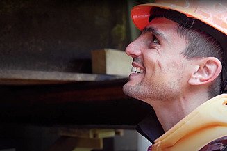 Bauführer mit orangen Helm lächelt während der Arbeit und schaut nach oben
