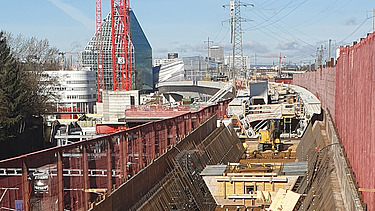  Ein Kran der STRABAG hebt nachts ein langes Brückenteil über Bahngleise. Die Baustelle ist hell erleuchtet.