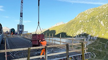 Ein Bauarbeiter von STRABAG bereitet den Betonkübel für den Brückenbau in der alpinen Landschaft vor.