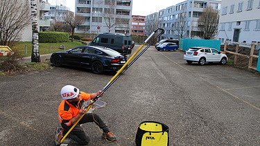 STRABAG Sicherheitsbeauftragter mit Wurfschleuder und Führungsseil auf einem Parkplatz. Im Hintergrund stehen einige Autos.