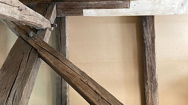 Blick in einen Dachstuhl mit Holzbalken und Verkleidung, links ist ein Gerüst zu sehen. Eine Kombination aus altem vorhandenem Holz mit neuem Holzelementen. 