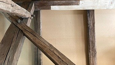 Blick in einen Dachstuhl mit Holzbalken und Verkleidung, links ist ein Gerüst zu sehen. Eine Kombination aus altem vorhandenem Holz mit neuem Holzelementen. 