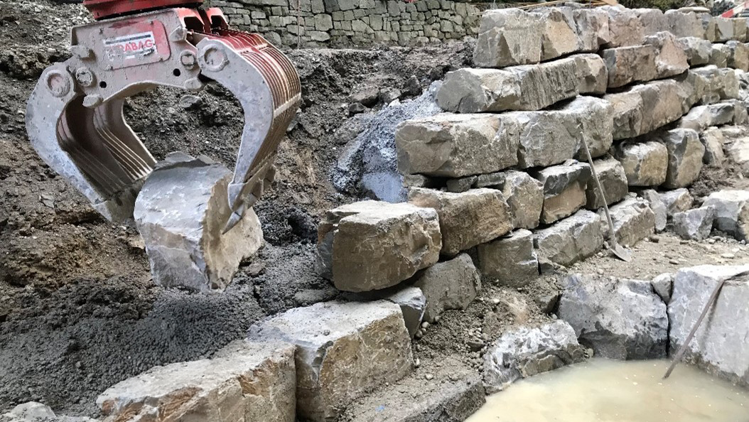 Foto von einer Krangreifer der einen Stein zu einer Mauer hebt