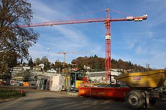 Sicht auf eine Baustelle mit grossem roten Kran und Baumaterial im Vordergrund.