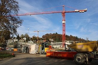 Sicht auf eine Baustelle mit grossem roten Kran und Baumaterial im Vordergrund.