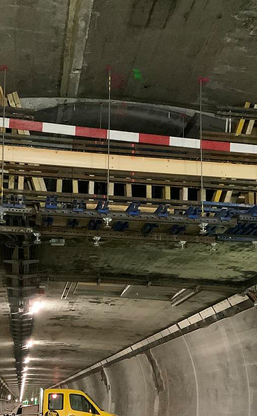 Nachtaufnahme einer STRABAG-Baustelle. Ein grosser Kran steht beleuchtet neben einem Wohnhaus unter dem klaren Nachthimmel.