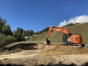 Schutz vor Naturgefahren - STRABAG Ingenieurbau Bagger der STRABAG am Aclettbach bei Disentis gräbt ein Fundament, im Hintergrund eine Eisenbahnbrücke