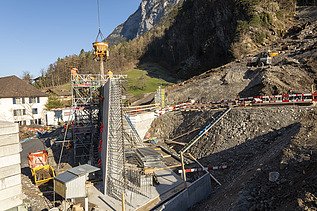 Bau einer massiven Betonmauer mit Kran, Gerüst und Maschinen zur Geländesicherung im Gebirge.