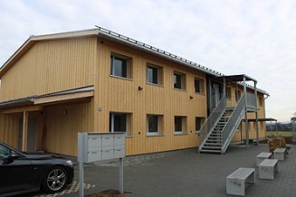 Asylunterkunft aus Holz, zweistöckig mit Metalltreppe und Geländer. 