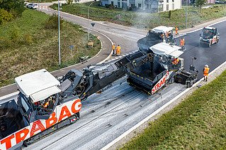 Ein Beschicker, zwei Fertiger, eine Walze und viele Bauarbeiter beim Asphalteinbau 