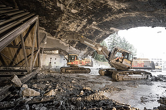 Zwei Bagger führen Abbrucharbeiten unter einer grossen Betonbrücke durch. Der Boden ist voller Schutt und Betonreste.