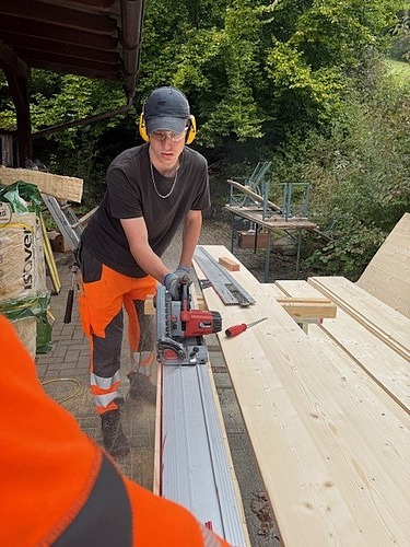 Blick von vorne auf einen Lernenden der gerade Latten mit der Kreissäge zusägt 