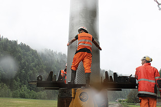 STRABAG Bauarbeiter in Warnkleidung steht auf einer Plattform und fixiert den Filterbrunnen. Im Hintergrund ist grauer Himmel und ein grüner Wald zu sehen.