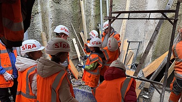 Kinder des Zukunftstags beobachten auf der Baustelle die Schalungsarbeiten für die Wände des zukünftigen Pumpwerks Scheller.