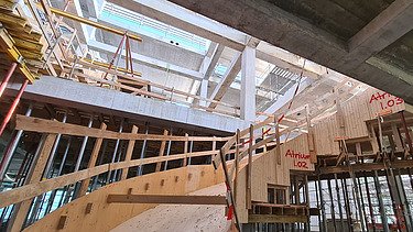 Zwei grosse Hebevorrichtungen auf einer STRABAG-Baustelle. Im Hintergrund sind Bauarbeiter:innen und ein Kran zu sehen.