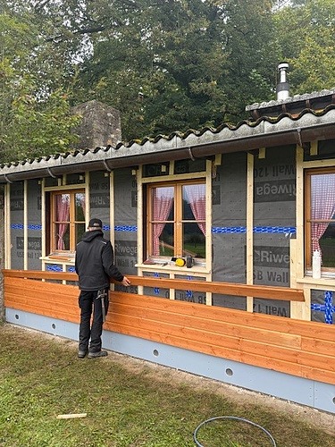 Blick auf die Holzfassade des Pfadiheims an der gerade ein Lernender dabei ist die neuen Holz Latten für die Fassade zusammenzustecken