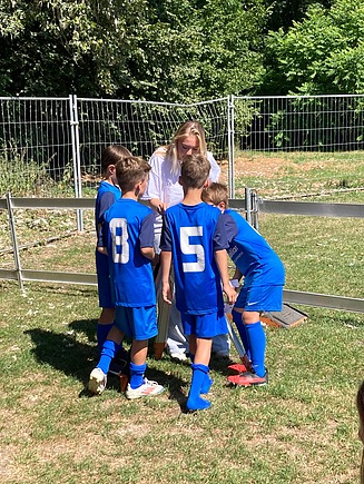 Eine junge Frau im STRABAG-T-Shirt zeigt einer Gruppe von Jungs in blauen Trikots das Nivellieren.