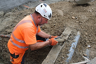 Ein Bauarbeiter mit orangefarbener Arbeitskleidung und weissem Helm legt ein eine alte Werkleitung frei 