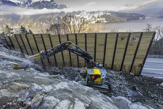 Gelber STRABAG Bagger steht in der Baugrube hinter einer Spundwand und spitzt Felsgestein ab