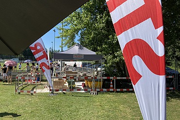 Festzelt von STRABAG auf einer grünen Wiese mit Baustellen-Simulation und Besucher:innen an einem sonnigen Tag.