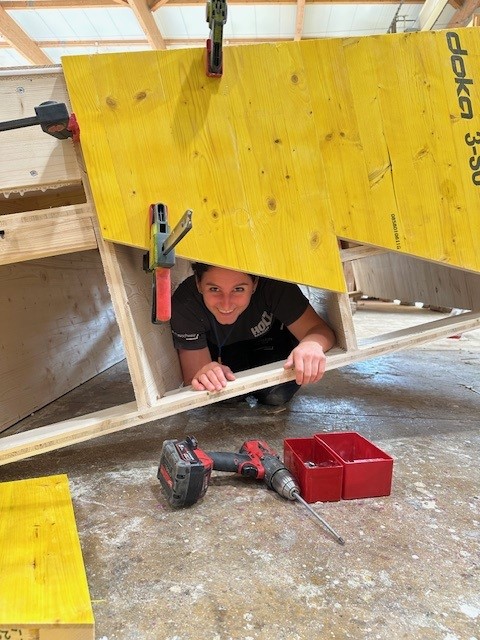 Zimmerin schaut durch einen Schlitz in der Schalung durch