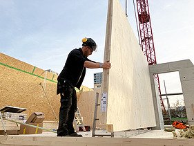 Einsetzen eines Holzelements durch einen Kran und einem STRABAG Mitarbeiter