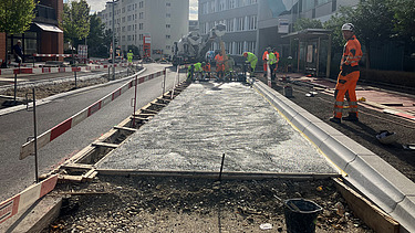 Zwei grosse Hebevorrichtungen auf einer STRABAG-Baustelle. Im Hintergrund sind Bauarbeiter:innen und ein Kran zu sehen.
