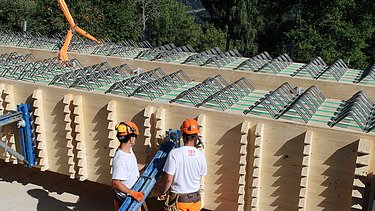 Zwei Arbeiter in Schutzkleidung richten einen frisch eingehobenen Holzträger millimetergenau aus