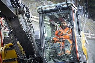 Nahaufnahme eines Baggerfahrers am Steuer eines Baggers in der Baugrube Axenstrasse