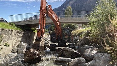 Arbeiten im Bach - STRABAG Ingenieurbau Bagger der STRABAG arbeitet direkt im Flussbett des Aclettbachs in Disentis unter einer Brücke.